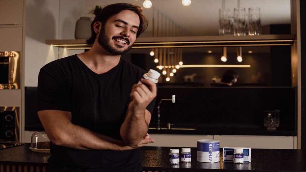 Homem sorridente analisando um frasco de suplemento natural em uma cozinha moderna.